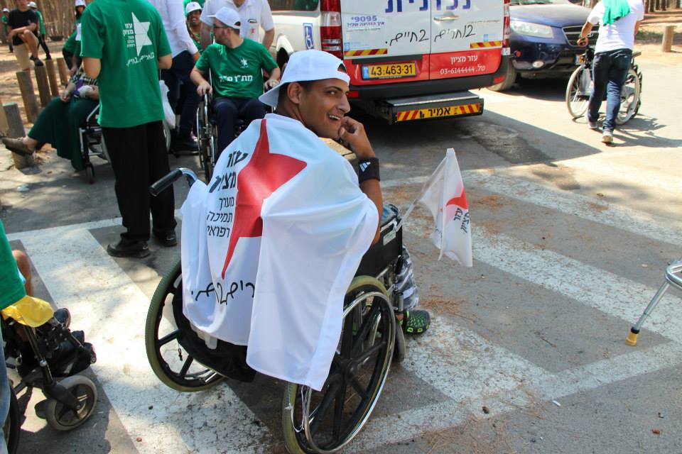 Ezer Mizion special needs summer campgoer in wheelchair with flag