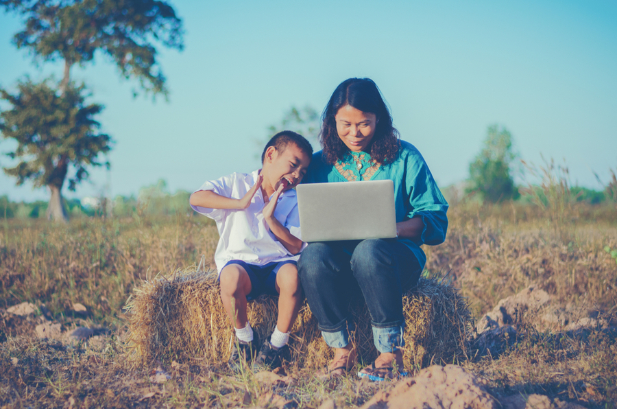 An Asian mom and son sitting outside at the countryside with a laptop showing that the mom could study at the university of the people while keeping her obligations to her family
