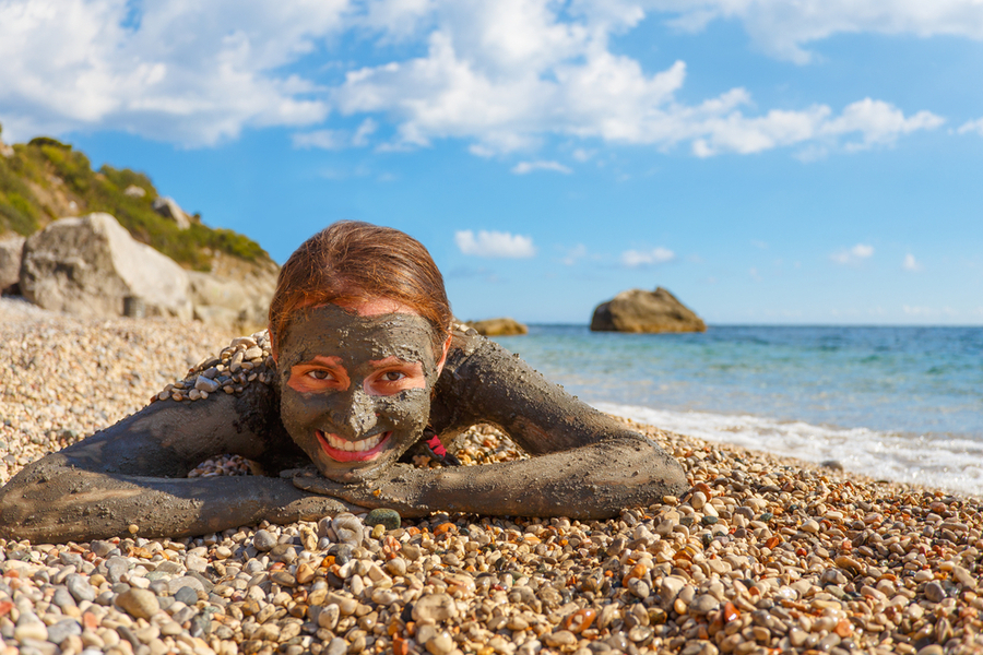 girl smiling with dead sea mud on her face lying down on the beach face front to the camera - israel